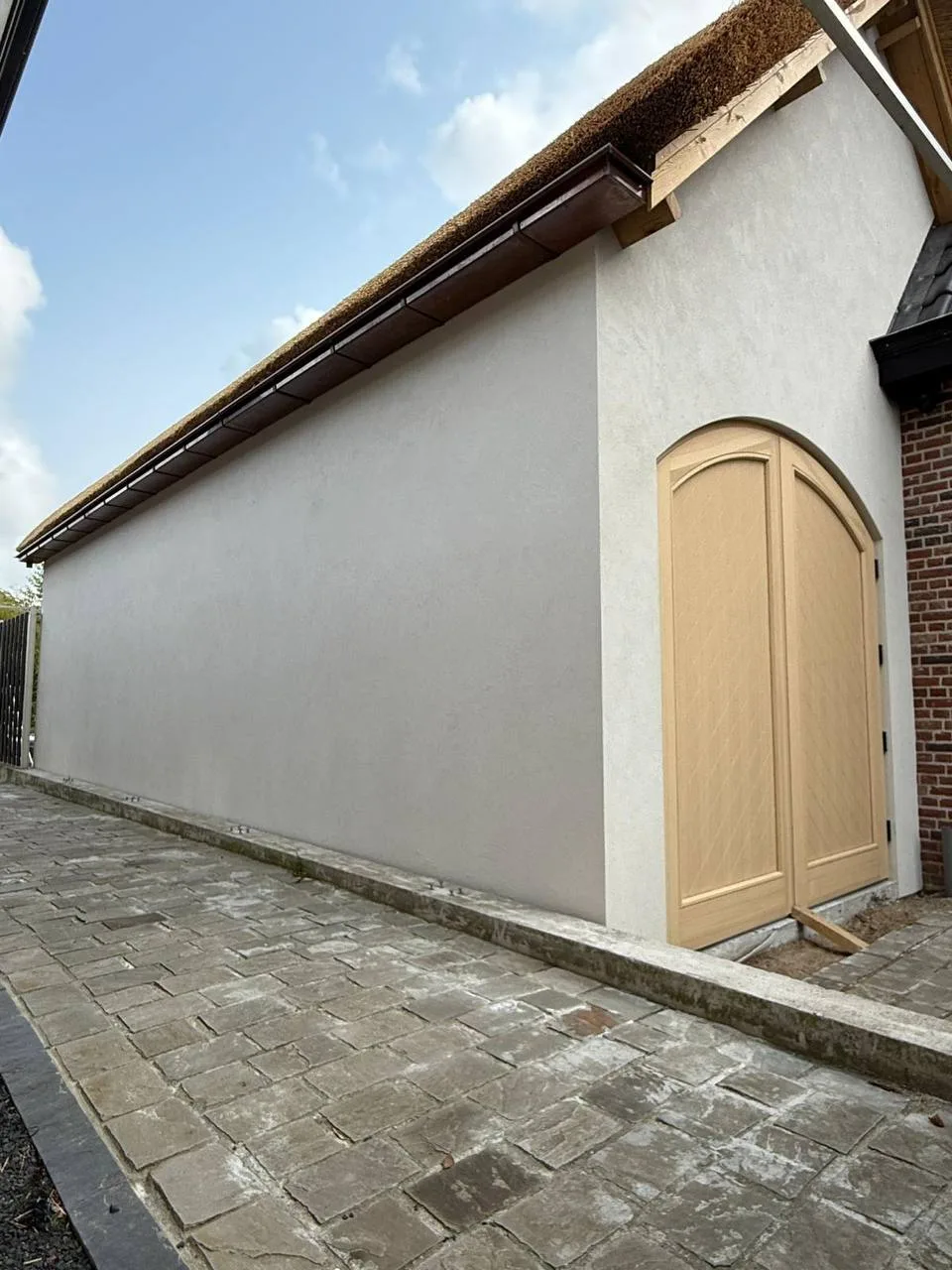 Lange gestuukte zijgevel met een eiken boogdeur aan het einde