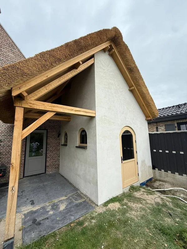 Gestuukt bijgebouw met een rieten dak, een houten overkapping en een boogdeur