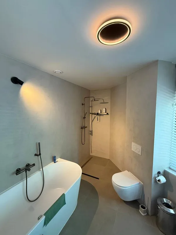 Badkamer met een bad, zwarte kranen en een plafondlamp, naast een raam met jaloezieën