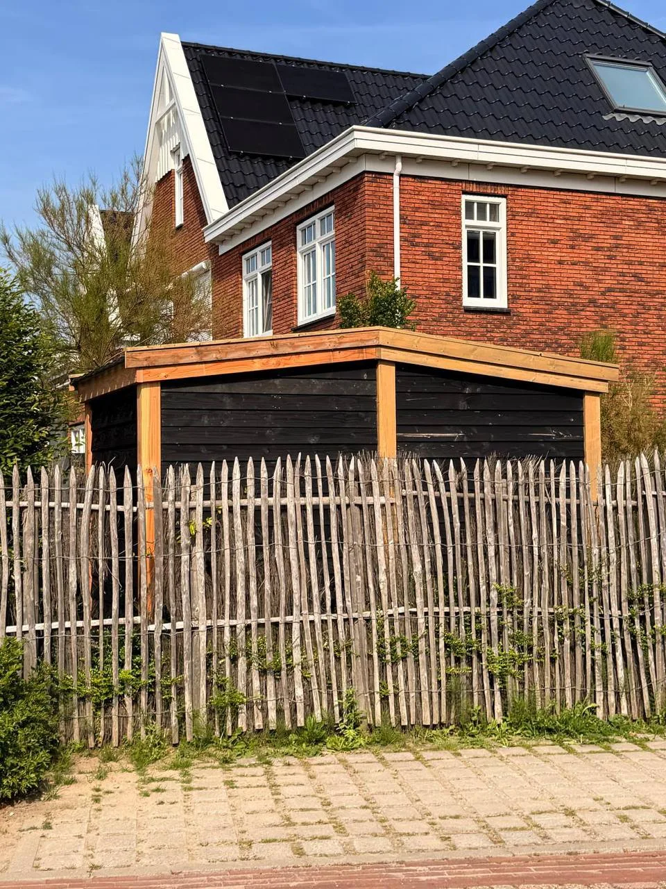 Dezelfde berging vanaf de straatkant, achter een houten hek