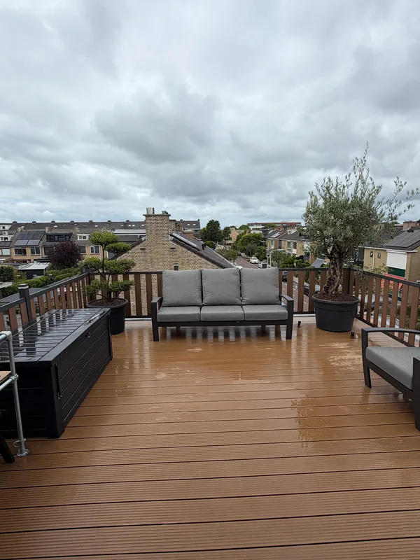Dakterras met houten vlonder, loungebank en plantenbakken, met uitzicht over de daken