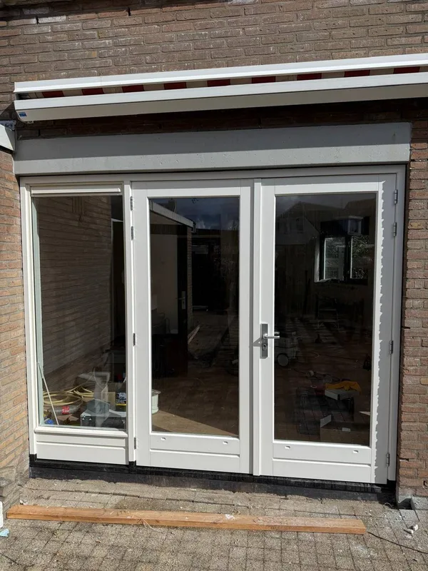 Nieuwe witte achterpui met openslaande deuren in een bakstenen gevel
