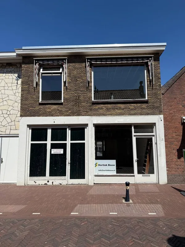 Voorpui van een winkelpand met witte kozijnen en glas, in een bakstenen gevel